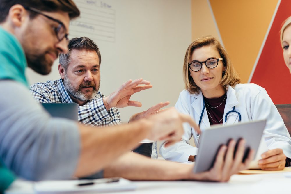 A group of clinicians meeting and looking at something on a tablet one is holding